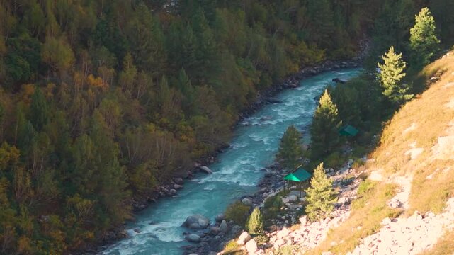 Slow motion shot of blue coloured Baspa river flowing in the forest in the Himalayas as seen from Chitkul in Kinnaur, Himachal Pradesh, India. Baspa river during the autumn season in the Baspa valley