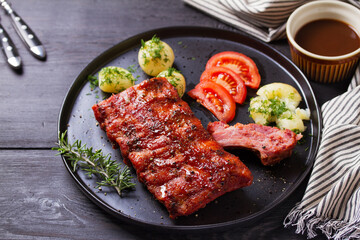 Rack of ribs with potatoes on black plate and coleslaw