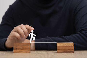 A close-up of a hand positioning a small figure on a wooden bridge, symbolizing teamwork and...
