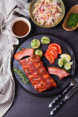 Rack of ribs with potatoes on black plate and coleslaw. View from above, top view