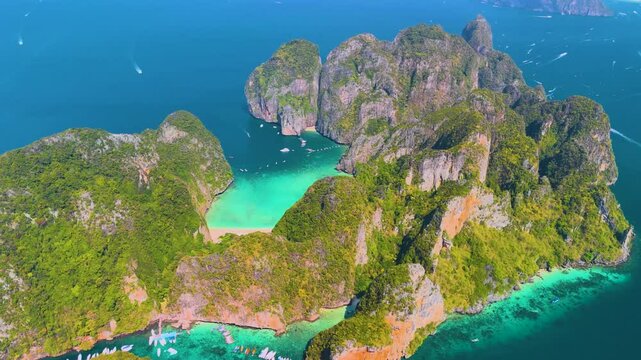 Aerial top panoramic beautiful frame approach view from afar of Phi phi island ring of steep limestone cliff hills surrounding Maya Bay white beaches and coral reefs around, boats floating nearby