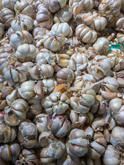 A pile of fresh garlic bulbs displayed in a market. The raw, unpeeled cloves showcase their natural texture and earthy tones, perfect for cooking, health benefits, and seasoning.