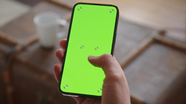 A hand is holding a Smart Phone with a Green Screen and Tracking markers at home. Also tapping and swiping.