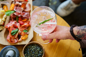 Hand holding cocktail with charcuterie platter in background