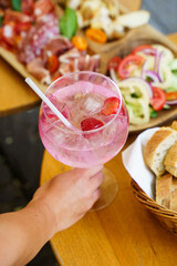 Hand holding cocktail with charcuterie platter in background