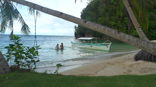 Tourists enjoying crystal clear water on a philippine beach near a traditional outrigger boat