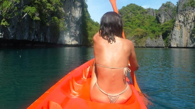 Young woman paddles an orange kayak through the stunning rock formations and turquoise waters of el nido, palawan