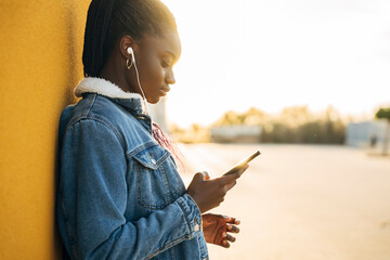 Stylish young woman enjoying music and using her phone outdoors