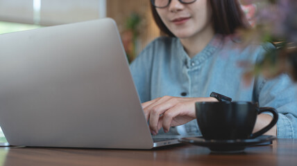 Fototapeta premium Young asian business woman working on laptop computer at coffee shop. Female freelancer online working on laptop with digital tablet on wooden table at cafe, online job, remote work