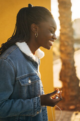 Young woman smiling and holding earbuds, enjoying music outdoors