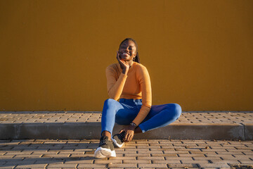 Young black woman smiling and relaxing against yellow wall