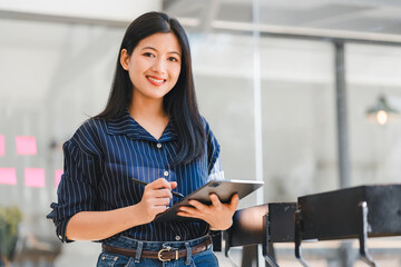 Confident Asian Businesswoman Holding Tablet and Stylus, Standing in Modern Office Environment.