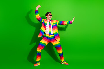 Young man wearing a rainbow striped suit on a green background, expressing happiness and energy. Vibrant colors representing pride