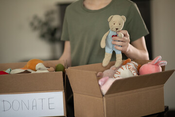 Cute teenager kid boy packing cuddly toys in the donation box at home.