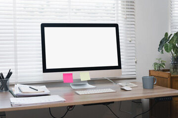 Fototapeta premium Modern Workspace With Computer Monitor, Keyboard, Sticky Notes, and Office Supplies on Wooden Desk Near Window With Blinds.