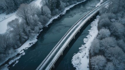 Aerial view of the bridge spanning the river, with the water frozen and covered in ice and snow. Aerial perspective of a snowy landscape. Road in the forest over the river.
