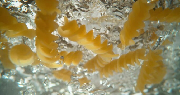 Pouring short penne macaroni pasta to a pan with boiling water in slow-motion. Organic healthy Mediterranean food