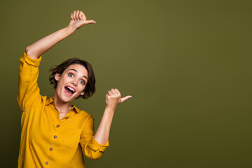 Portrait of a joyful young woman in a yellow shirt gesturing excitedly against a green background