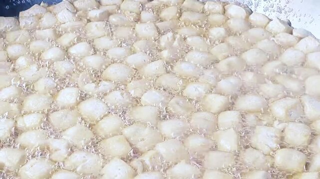 Cinematic shot. The cooking process of Tofu being deep-fried, likely for a dish called Crispy Pong Tofu, a popular Indonesian street food