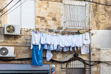 White laundry, hoodies, T-shirts, sweaters, and duvet covers hang on lines under a house window to...