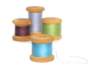 Old retro sewing colored thread spools blue one in front of others isolated on white