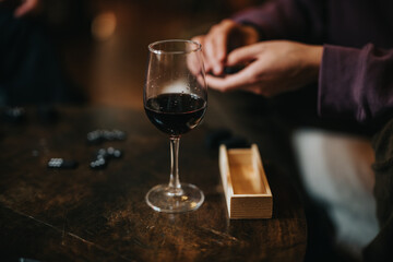 A glass of red wine beside a table of domino pieces, symbolizing leisure, strategy, and social interaction in an intimate setting.