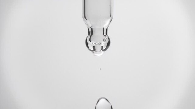 Cosmetics transparent liquid dripping from laboratory glass pipette in super slow motion. Macro shot of drop hanging down from chemical dropper. Abstract body care serum ingredients concept