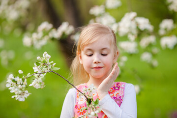 Fototapeta premium Little blonde girl admiring a blooming apple tree branch in a spring garden