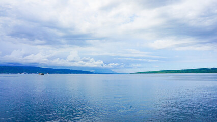 Obraz premium Expansive Ocean View with Green Coastline and Distant Mountains Under a Cloudy Sky