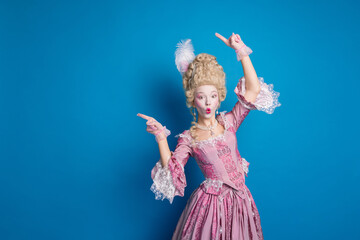 Elegant woman in pink Baroque costume with funny expression against vibrant blue background