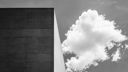 A stark, concrete structure reaches skyward, its clean lines and sharp angles juxtaposed against a soft, billowy cloud. Sunshine enhances the dramatic interplay between hard edges and soft forms