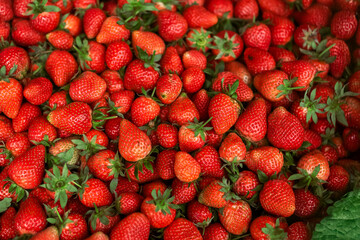 Fresh ripe strawberries with green leaves, piled together in a market setting. Vibrant red color and juicy texture, perfect for food, health, and organic produce concepts.