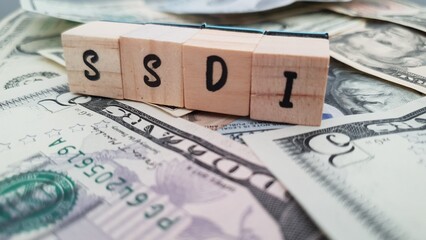 SSDI acronym made of wooden letter cubes on pile of US dollar banknotes. Social Security Disability...