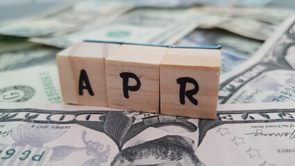 APR acronym made of wooden letter cubes on pile of US dollar banknotes. Annual Percentage Rate
