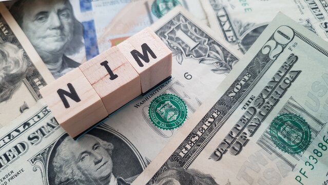 NIM acronym made of wooden letter cubes on pile of US dollar banknotes. Net Interest Margin