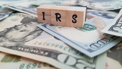 IRS acronym made of wooden letter cubes on pile of US dollar banknotes. Internal Revenue Service