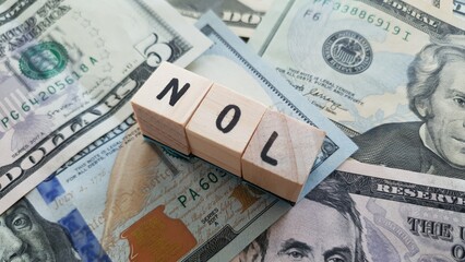 NOL acronym made of wooden letter cubes on pile of US dollar banknotes. Net Operating Loss