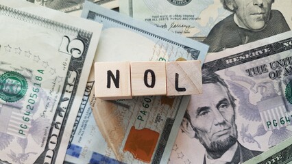 NOL acronym made of wooden letter cubes on pile of US dollar banknotes. Net Operating Loss