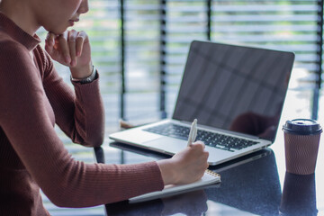 Young Asian woman working on laptop in a relaxed cafe area.