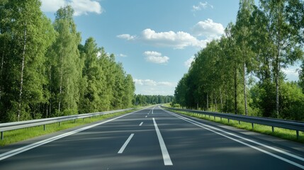 Obraz premium Scenic view of an empty highway lined with lush trees under a clear blue sky in a rural area during daytime