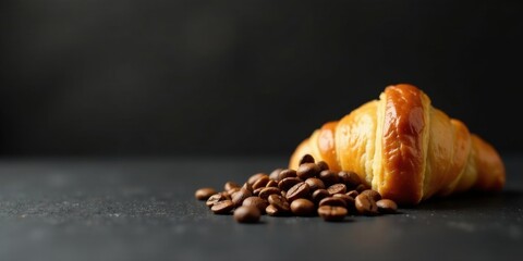 A freshly baked croissant rests beside a scattering of aromatic coffee beans on a dark surface, a tempting image of breakfast delights