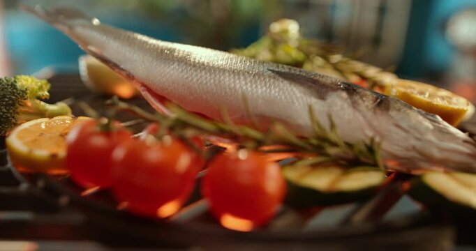 Dropping sea bass fish on the fire grill around vegetables, preparing sea food in the restaurant. Slow-motion footage