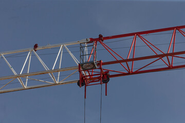 A vividly colored red and white construction crane stands tall against a clear blue sky, showcasing its mechanical structure and design