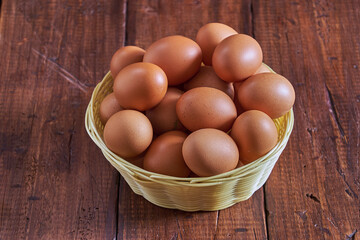 Raw brown eggs arranged in a basket with a rustic wooden background