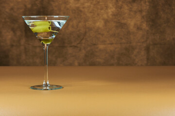 Refreshing Martini glass with green olives inside, on a warm colored surface.