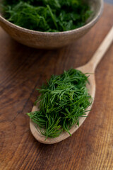 Concept of aromatic herbs for cooking. Chopped fresh dill with a wooden spoon on a brown kitchen board background. Preparing to freeze. © pyansetia2008