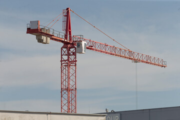 A striking red and white construction crane is prominently positioned at the top of a tall...