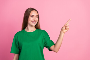 Young woman in green t-shirt pointing with her hand against pink background, conveying a casual and...