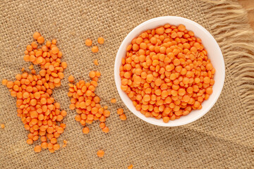 Red lentils in a ceramic plate  on a jute napkin, close-up, top view.