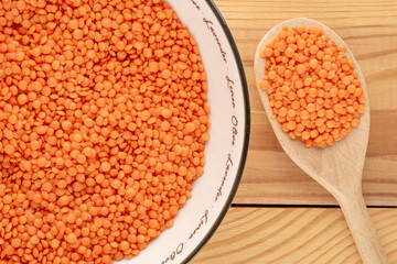 Red lentils in a ceramic plate with a wooden spoon on a wooden table, close-up, top view.